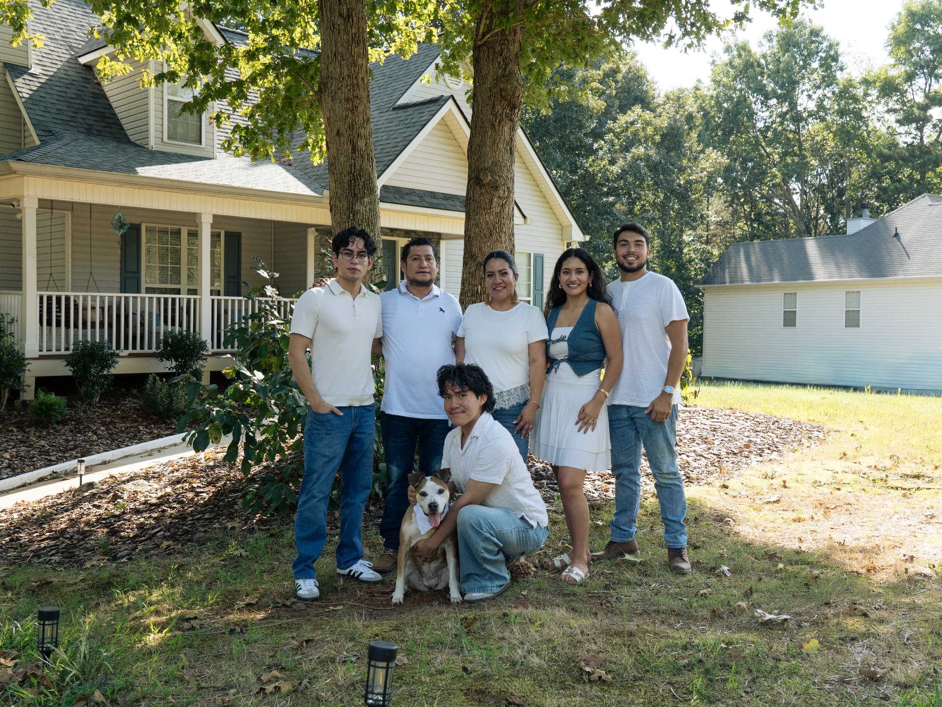 Family portrait with five relatives and their dog together in a sunlit yard
