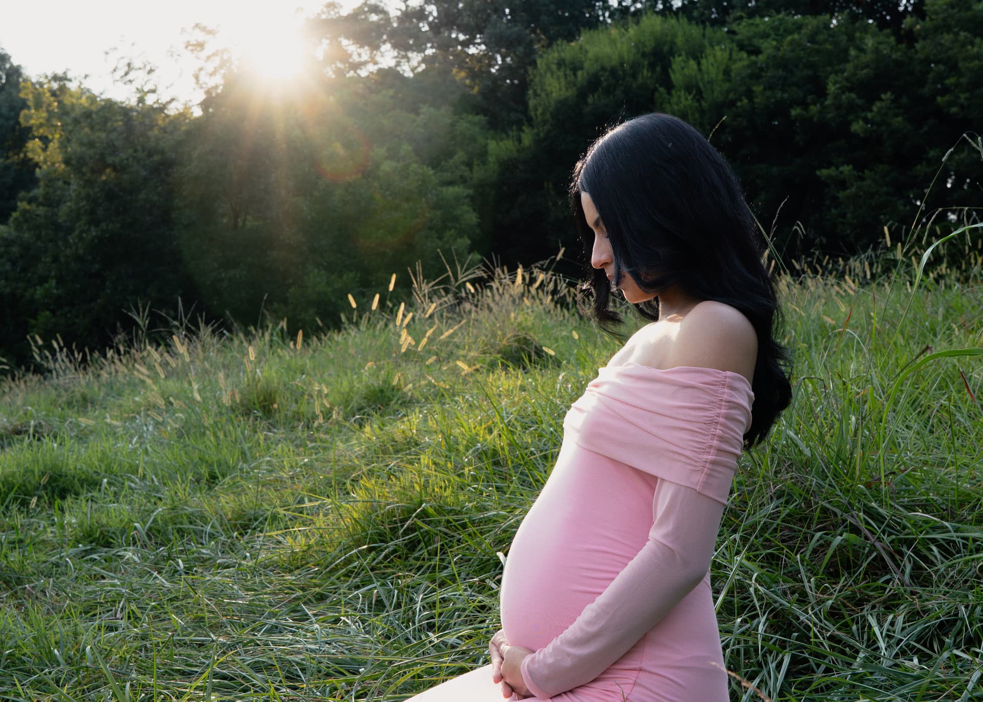 Maternity portrait of an expecting mother in a pink gown in a sunlit meadow in North Georgia